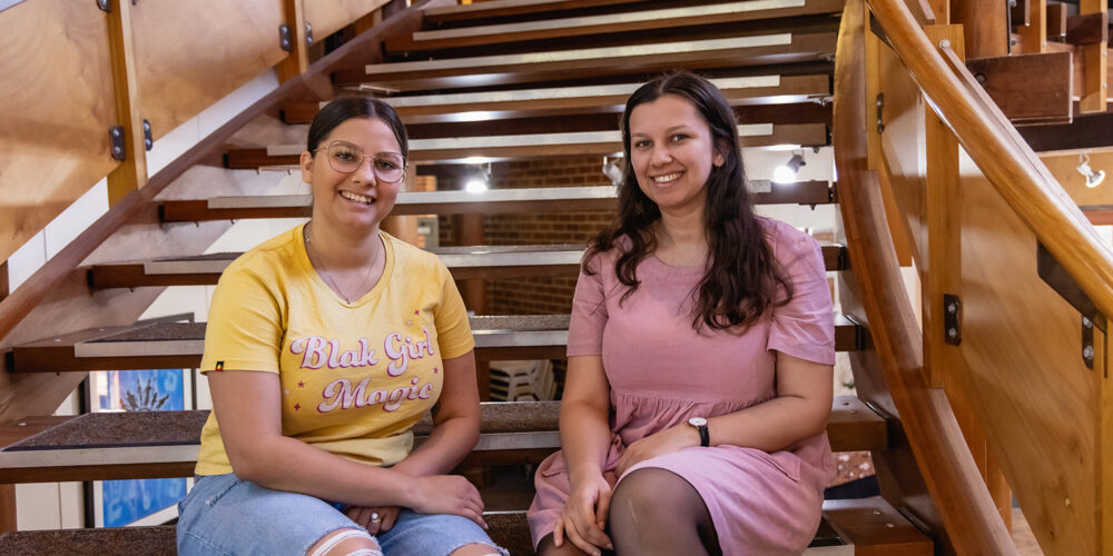 Two Indigenous students sitting on the CAS stairwell and smiling at the camera