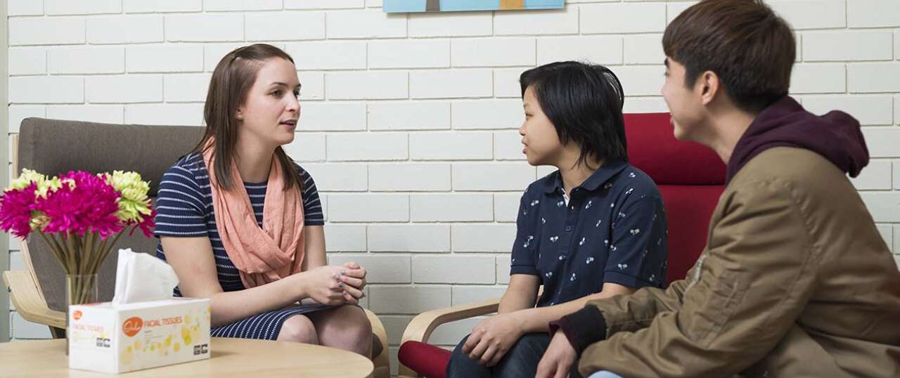 A student in her twenties talks to two younger boys in a professional setting.