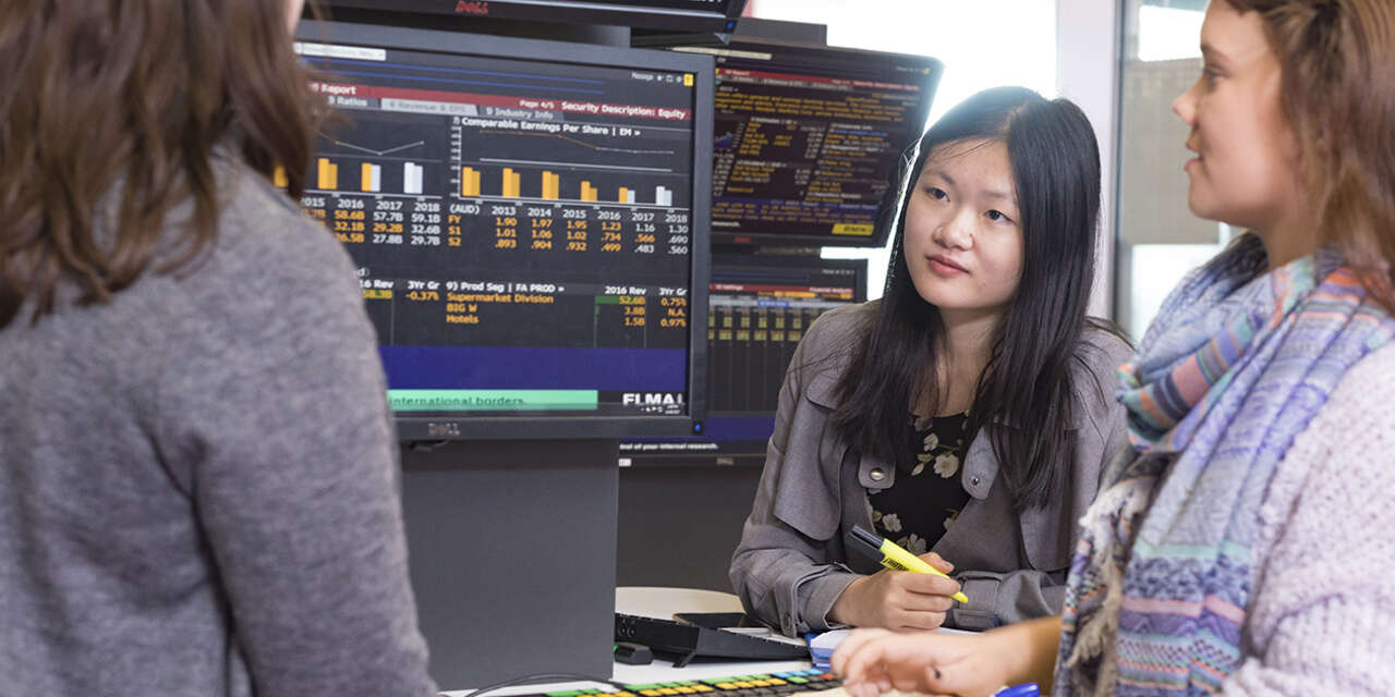 University students looking at computer screens that show stock trading data.