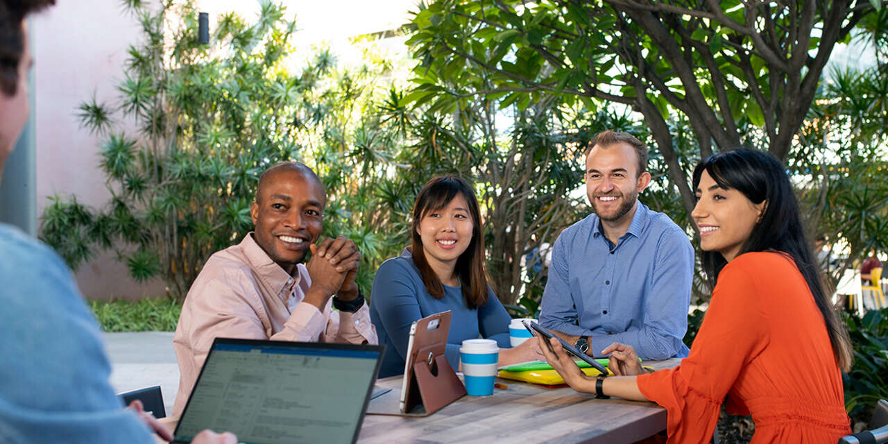 Four students sitting at a table smiling at someone sitting on a laptop out of shot.
