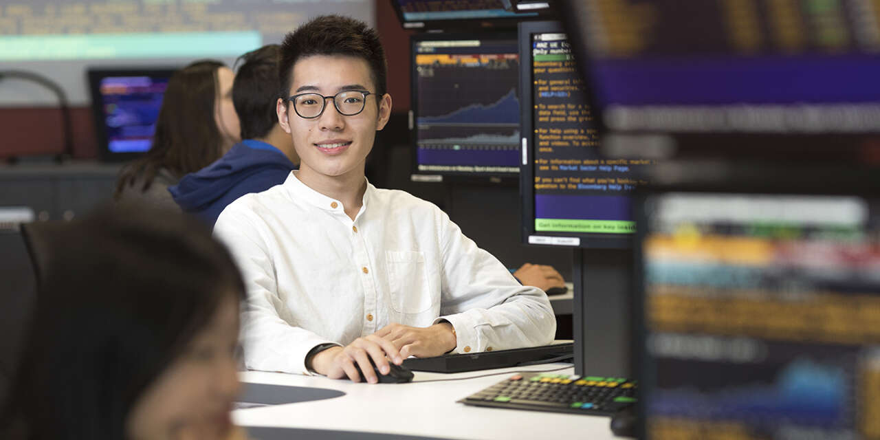 Student sitting in in front of computers that show trading information on the display.