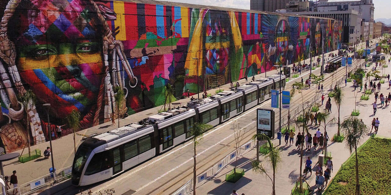 Trams circulating through busy town centre with large colourful mural in the background.