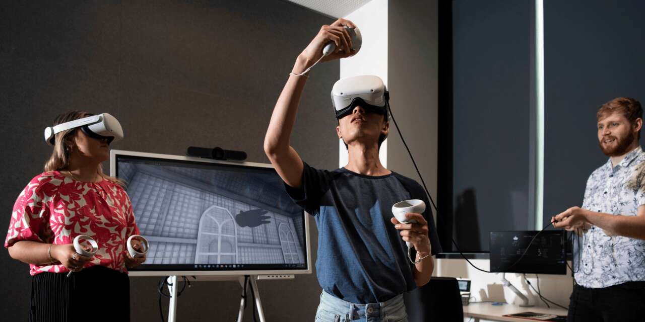 A woman and a man wearing headsets immersed in virtual reality with one person in the background.