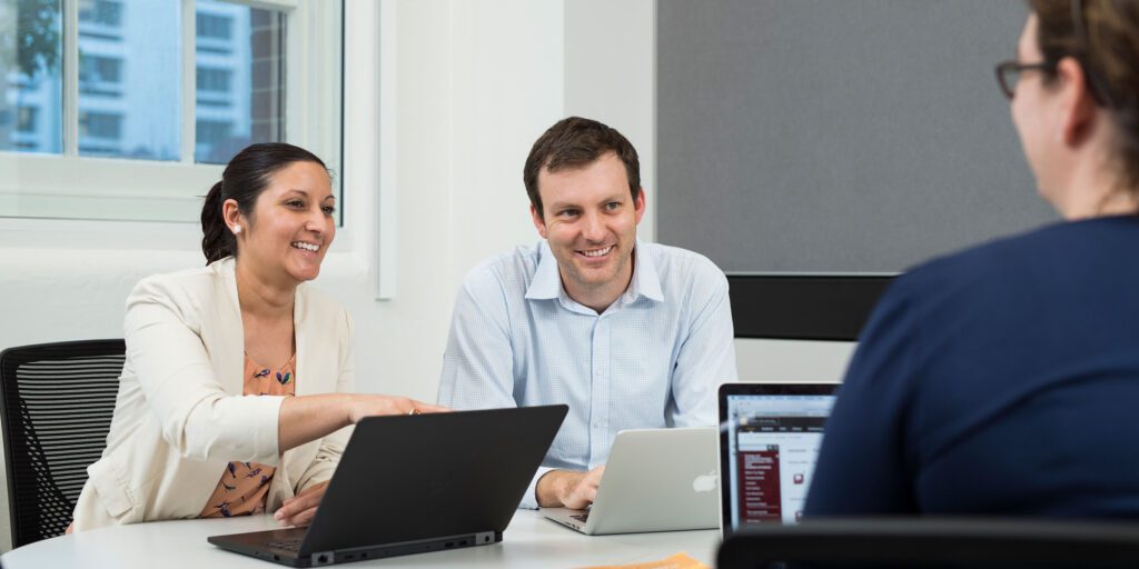 Three Curtin staff members sitting at a table using laptops