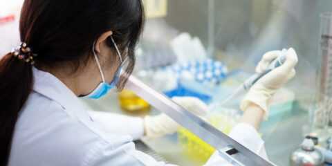 A student in a laboratory performing a safe pipetting technique in a biosafety cabinet.