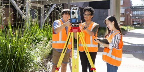 Three students in reflective clothing using surveying equipment