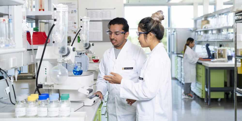 Two students in a laboratory wearing a laboratory coat and safety glasses