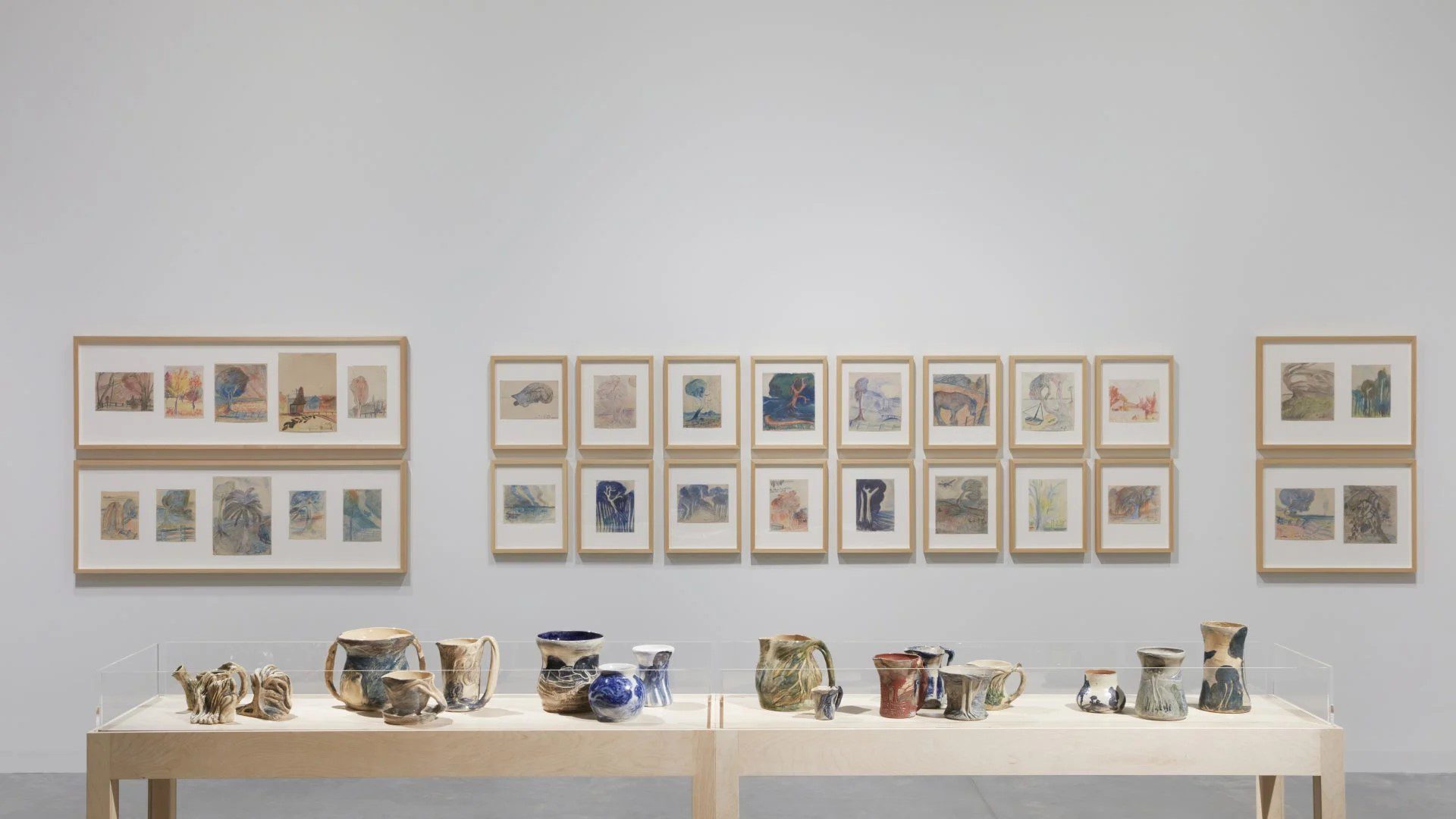 A table containing ceramics infront of a series of framed artworks along a gallery wall.