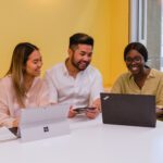 3 students sitting a desk with laptops