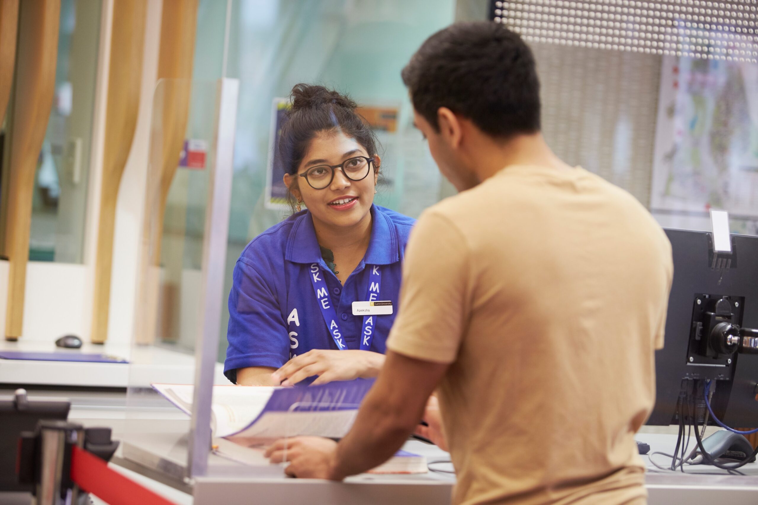 A library staff member helps a student at the library help desk