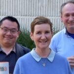 Dr Hendra Gunosewoyo, Catherine Clark (University Librarian) and Dr Alan Payne stand outside in front of bushes holding mugs that say