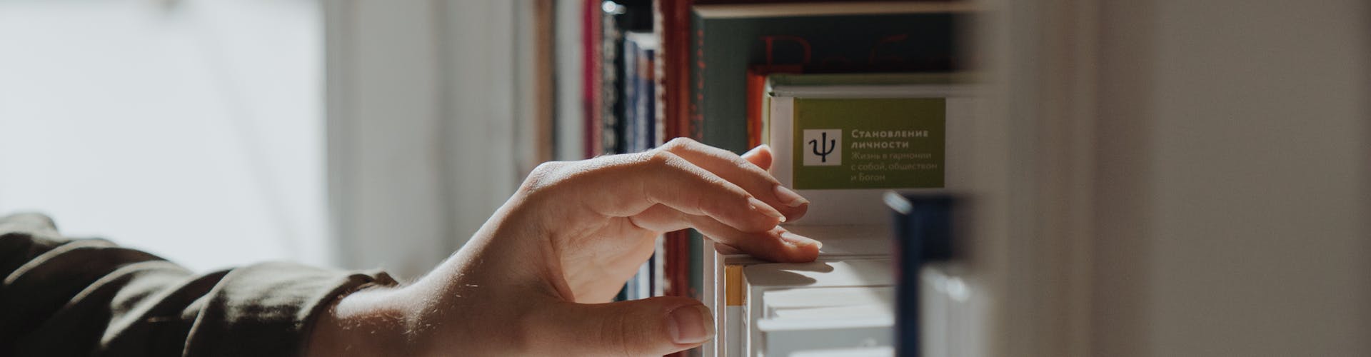 A hand reaches out to select a book from a well-arranged indoor bookshelf.
