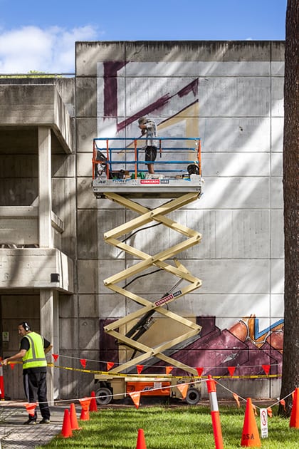 Two artists work on their murals outside.