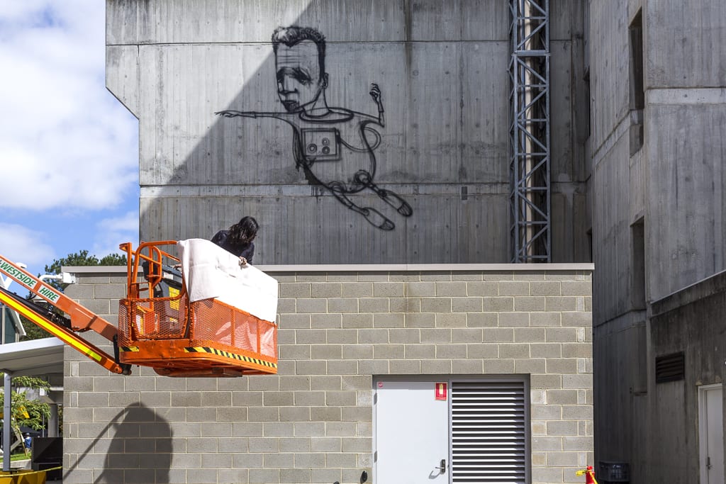 Artist in cherry picker with developing artwork of an astronaut in background.