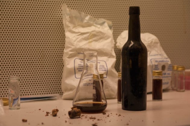 A beaker containing some of the bottle's contents, and its disintegrated cork in the foreground. 