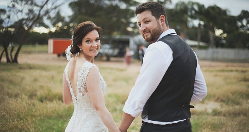 Kate and Luke hold hands in a wheat field.