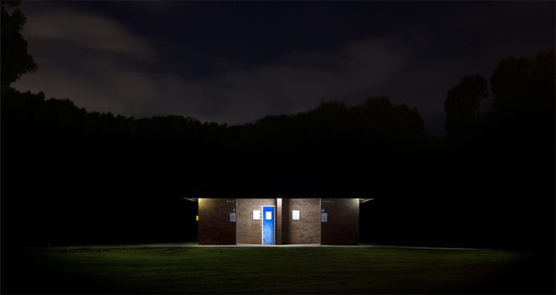 Underexposed shot of a toilet block at night, with the lights of the block illuminating the male and female entrances. 