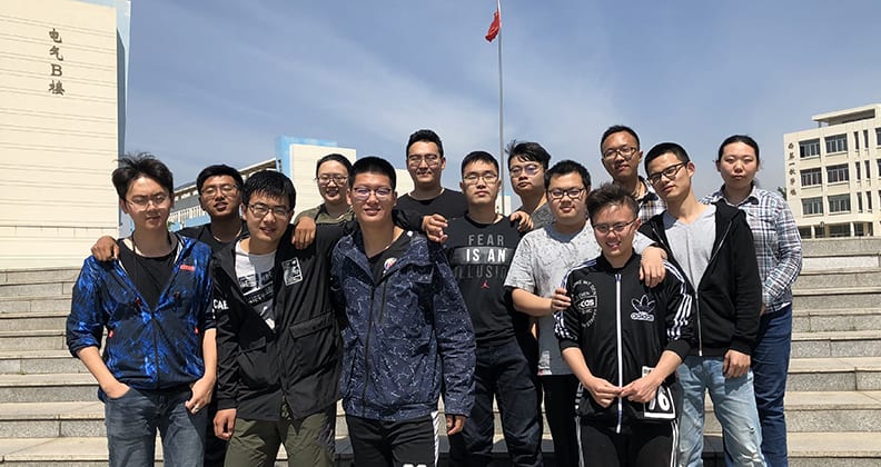 Postgraduate students from Yanshan University standing in their hometown in front of a flag and buildings.