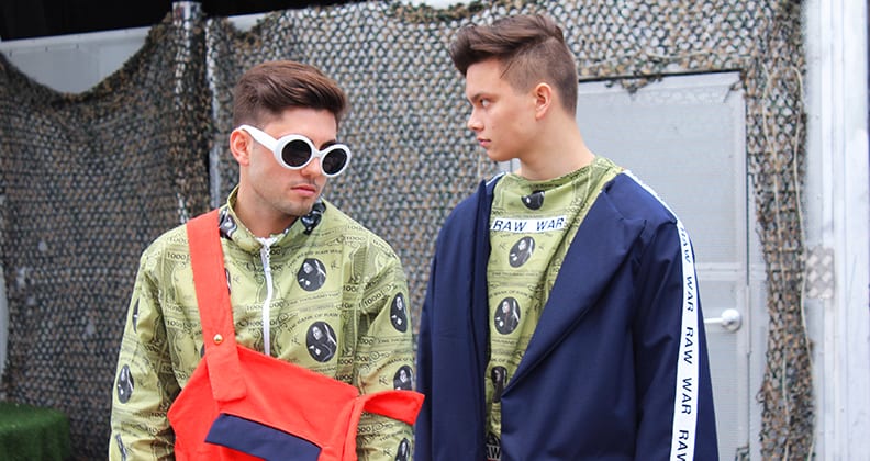 Two young boys stand together wearing green jackets with a stylised US dollar bill print. 