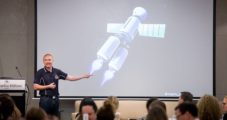 Josh Richards gives a presentation in front of a screen displaying a space shuttle concept. 