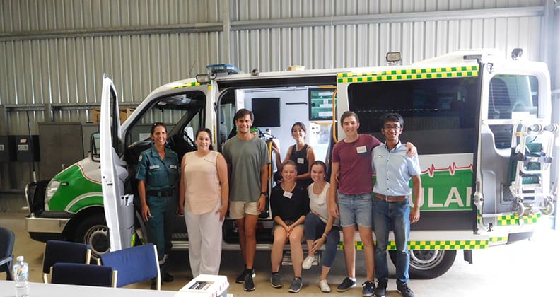 Healthcare workers posing for a photograph in front of an ambulance in a shed.