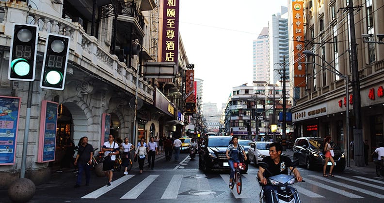 A lively Shanghai street scene with people riding bikes and cars navigating through the busy city environment.
