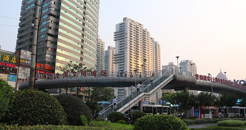 A street bridge in Shanghai overlooks a busy road, with a tall building rising in the background.