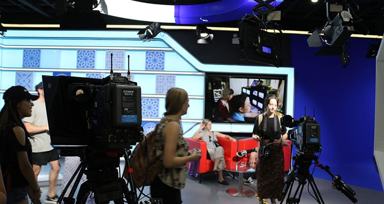 A television studio filled with journalism students working in front of cameras, engaged in a live broadcast setup.