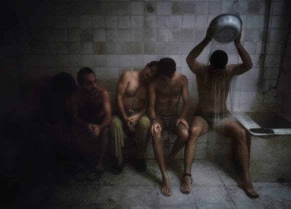 Five men rest quietly in a dimly lit white-tiled old bathroom