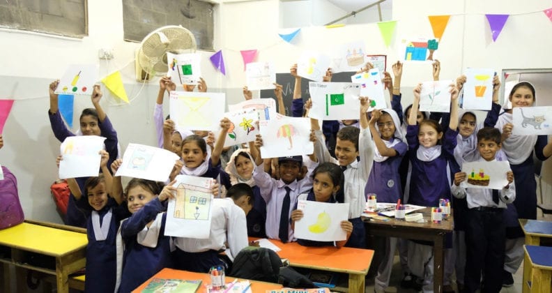 Girls from Anum School in Karachi, Pakistan, proudly display their artwork in a classroom.