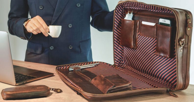 Man in suit holds espresso cup and showcases a leather briefcase with a red and white striped lining.