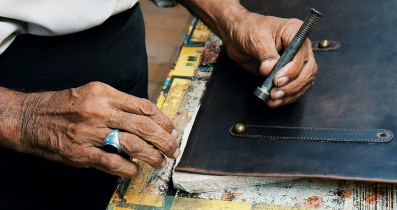 Close-up image of hands working on a piece of leather. 