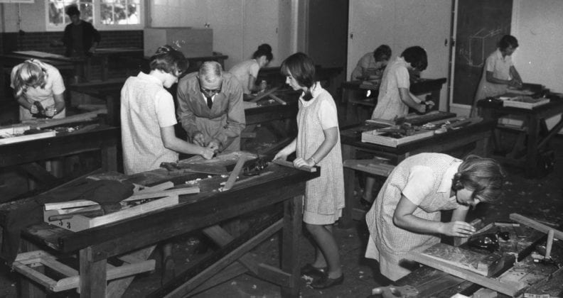 A black and white photograph of female students practising wood work skills in a workshop.