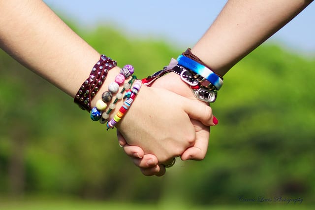 Two people holding hands wearing colourful bracelets