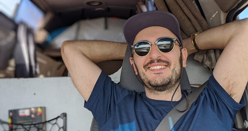 Gougoulis in sunglasses and cap learning back in a car seat. 