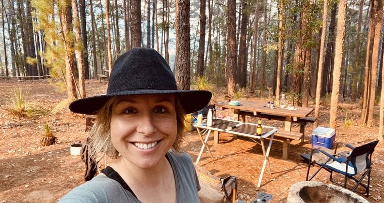 A selfie of Vanessa Rauland and her camp site among pine trees.