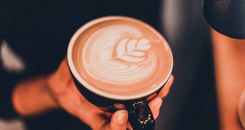 Close up shot of a hand holding a cup of flat white.