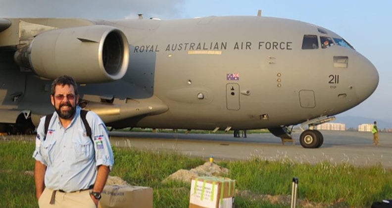Dr Robertson stands in front of a massive Royal Australian Navy Air Force plane, surrounding by packing boxes.