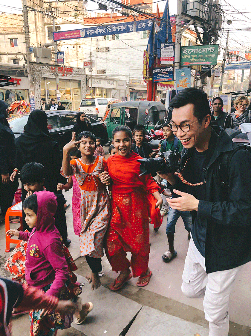 Marcus Wong with a camera walking down a busy street in Bangladesh