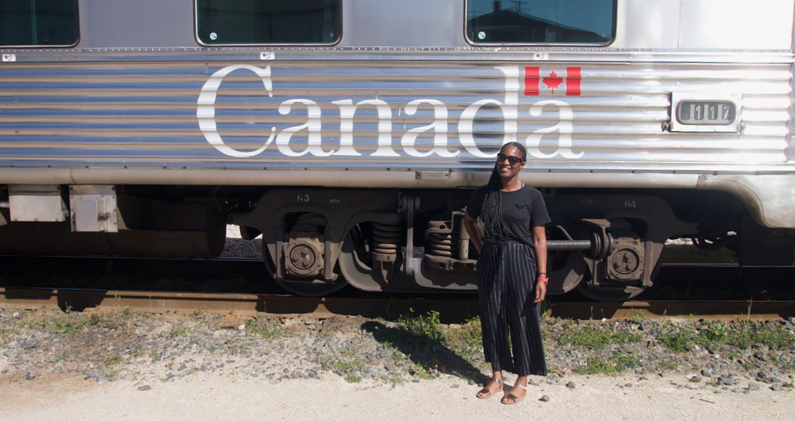 Abby Asomani stands in front a train with the words 'Canada' written on the side and the Canadian flag. 