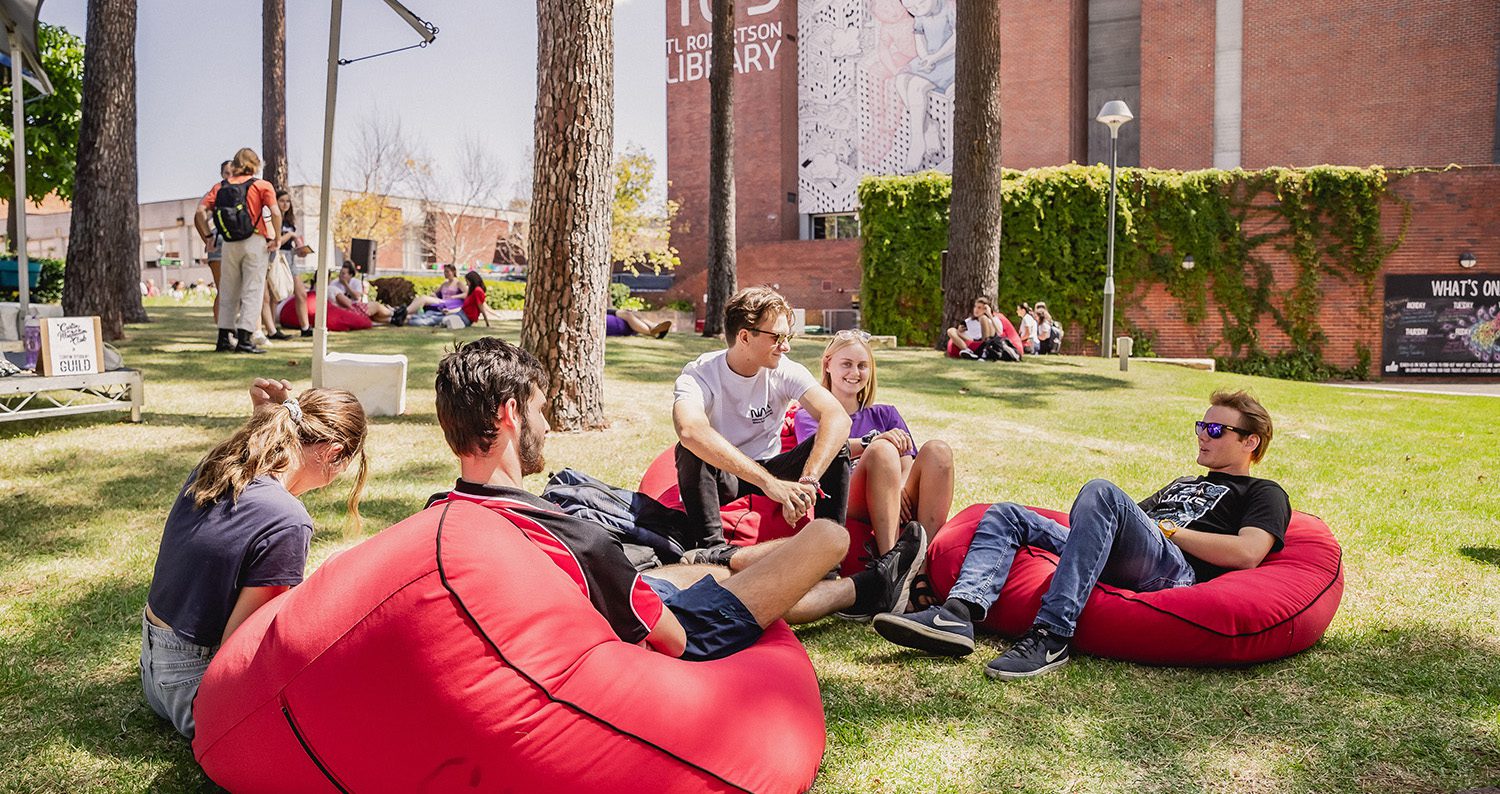 Group of students sitting on red bean bags at Henderson Court under the pine trees