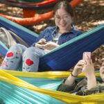 Two female students sitting on hammocks at The Hammock Hotel on campus.