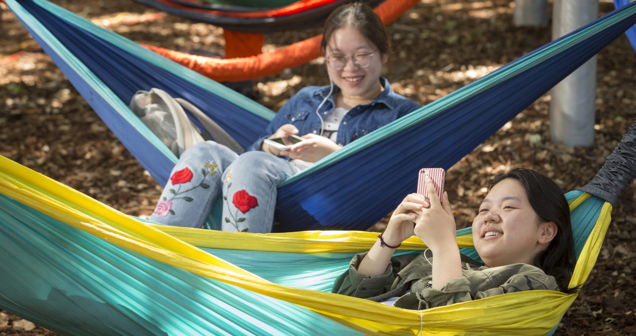 Two female students sitting on hammocks at The Hammock Hotel on campus.