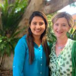 Anjali and Nina stand together and smile at the camera.