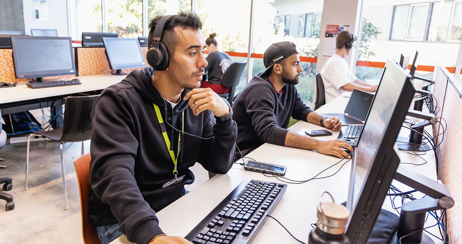 A male student wearing headphones, sitting at a desk and using a computer