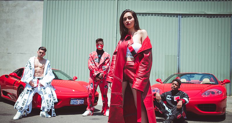 A young woman stands in the foreground wearing a bright red, full-length leather jacket, white tube top and red leather shorts. Behind her are three men in urban street wear, posing in front of Ferrari cars. 