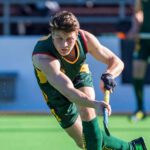 Hayden plays hockey on a field. He wears Australian green and gold.