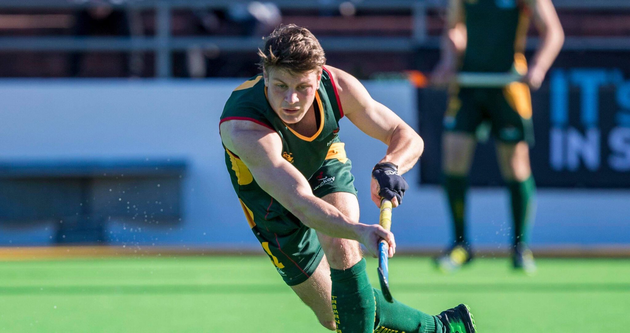 Hayden plays hockey on a field. He wears Australian green and gold.