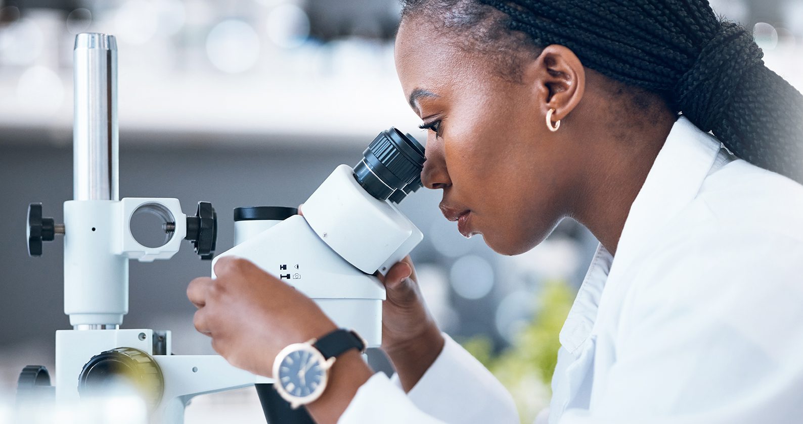 Woman looking into a microscope in a medical lab setting.