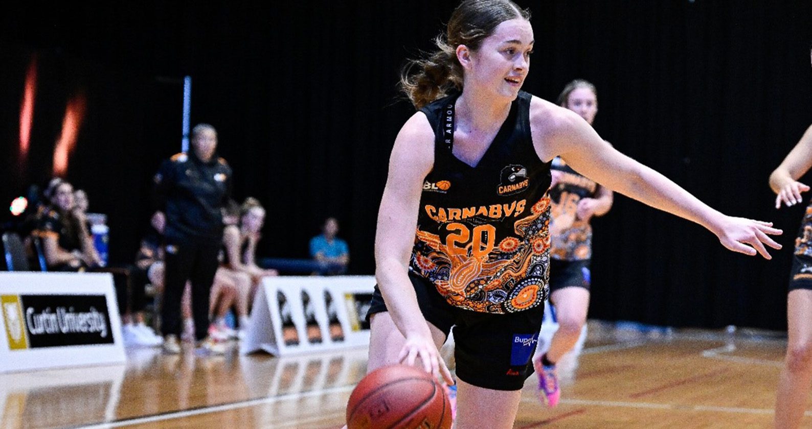 A female student basketball player bouncing a basketball.